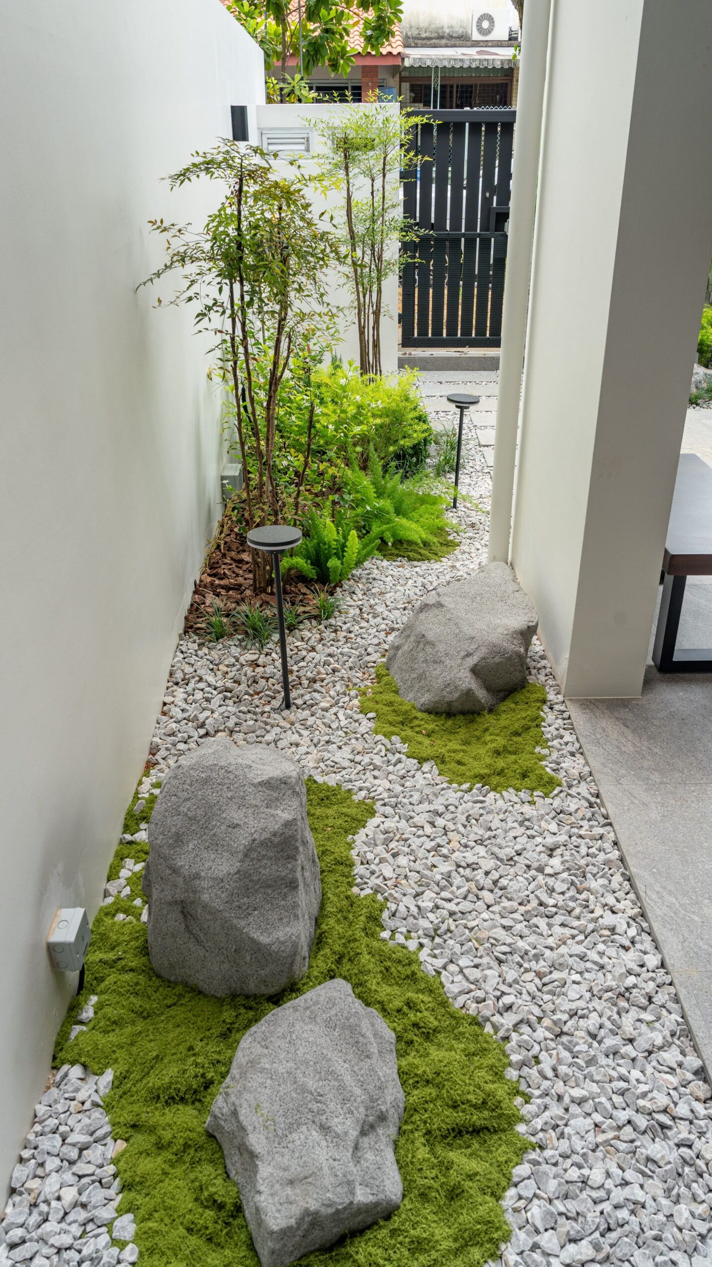 Individual boulders surrounded by patches of green groundcover within a narrow gravel garden.